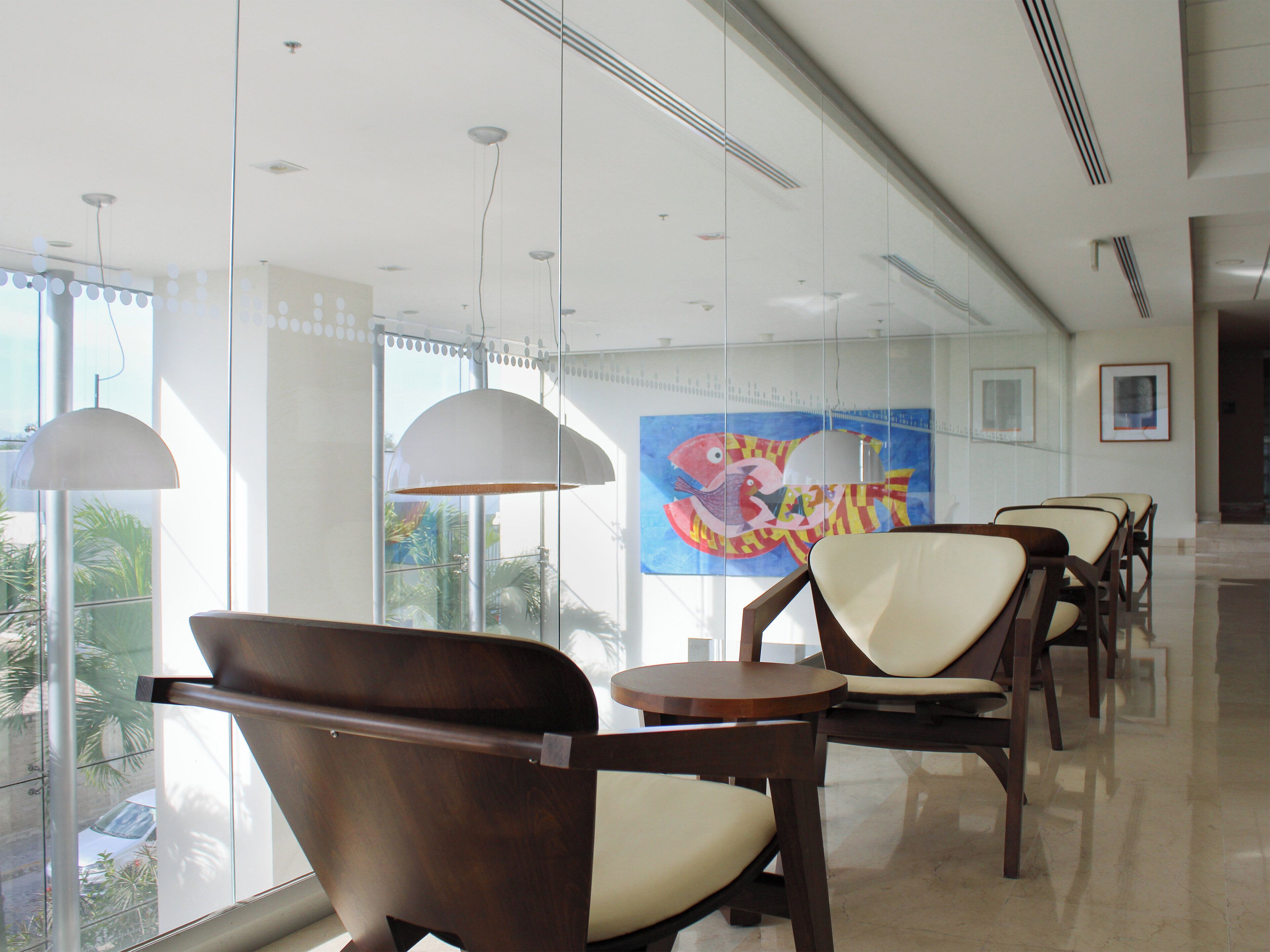 A modern hotel lobby with glass walls, wooden chairs, and a large colorful mural on the wall.