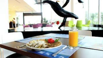 A dining table with a plate of food, a glass of orange juice, and a menu.