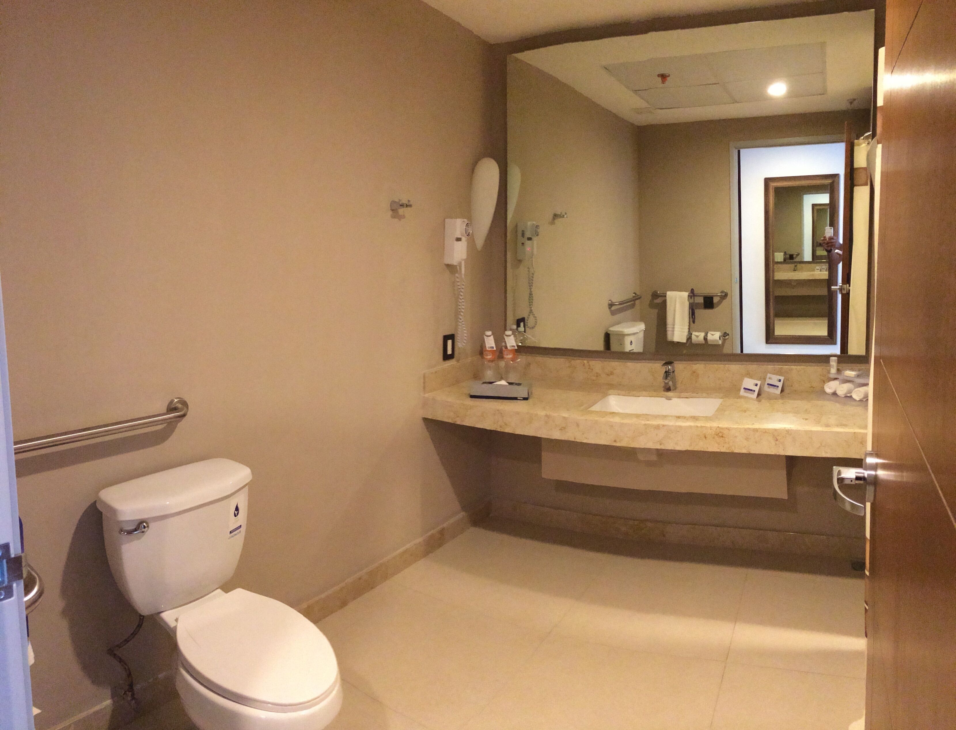 A bathroom with a toilet, a sink, a mirror, and a hand dryer.