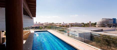 A rooftop swimming pool with a glass railing, surrounded by buildings and a clear sky.