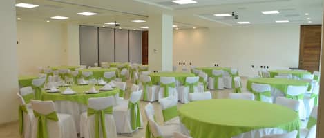 A conference room with multiple tables and chairs, each with a green tablecloth and white chair covers tied with green sashes.
