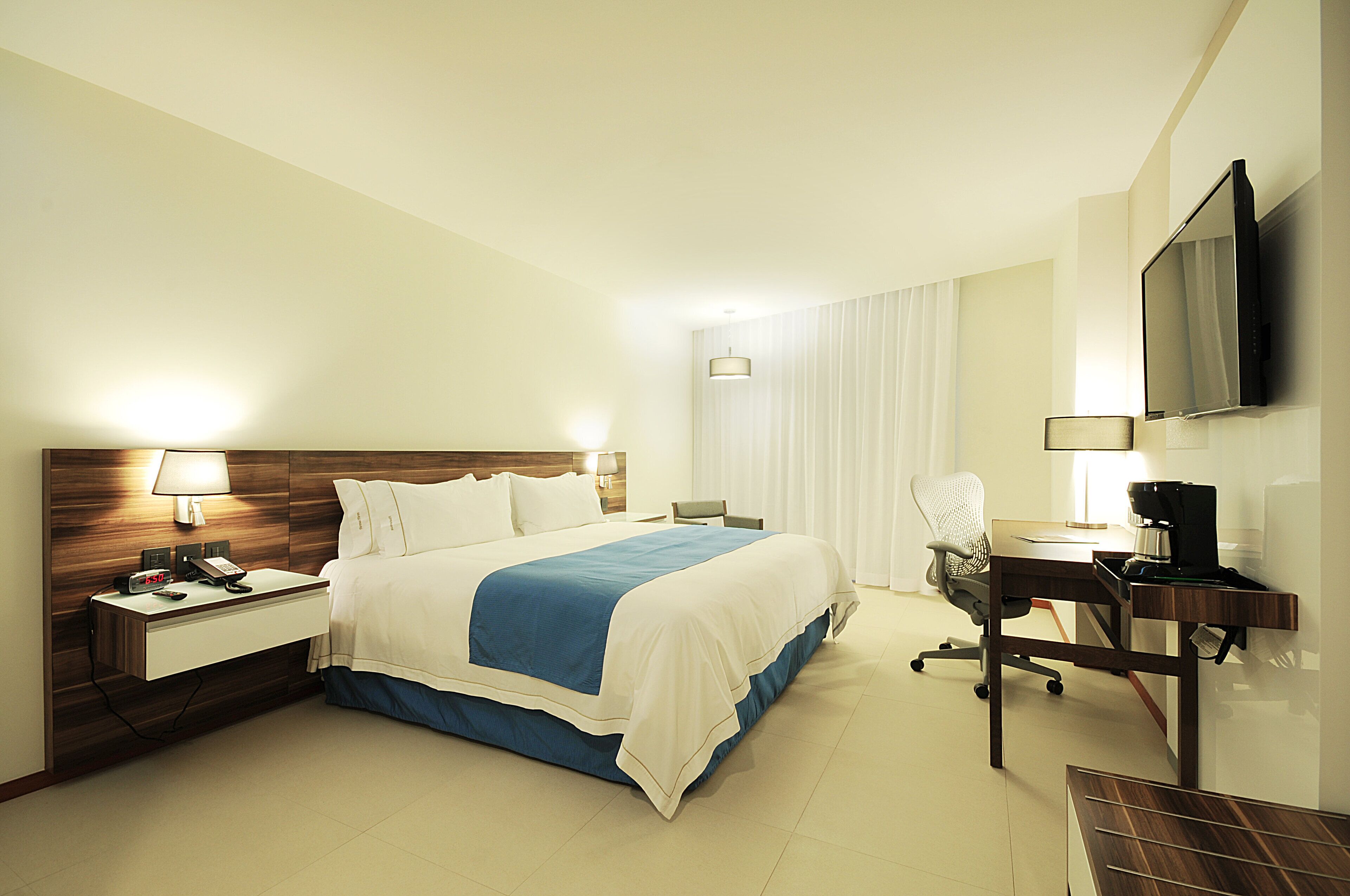 A hotel room with a bed, desk, chair, TV, and bedside lamps.