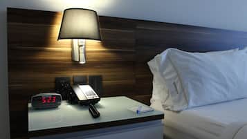 Ein Hotelzimmer mit Nachttisch, digitaler Uhr, Telefon, Lampe und einem Bett mit weißer Bettwäsche.
