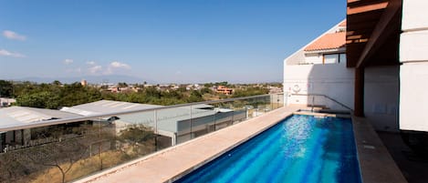 A rooftop swimming pool with a clear view of the surrounding landscape and distant buildings.