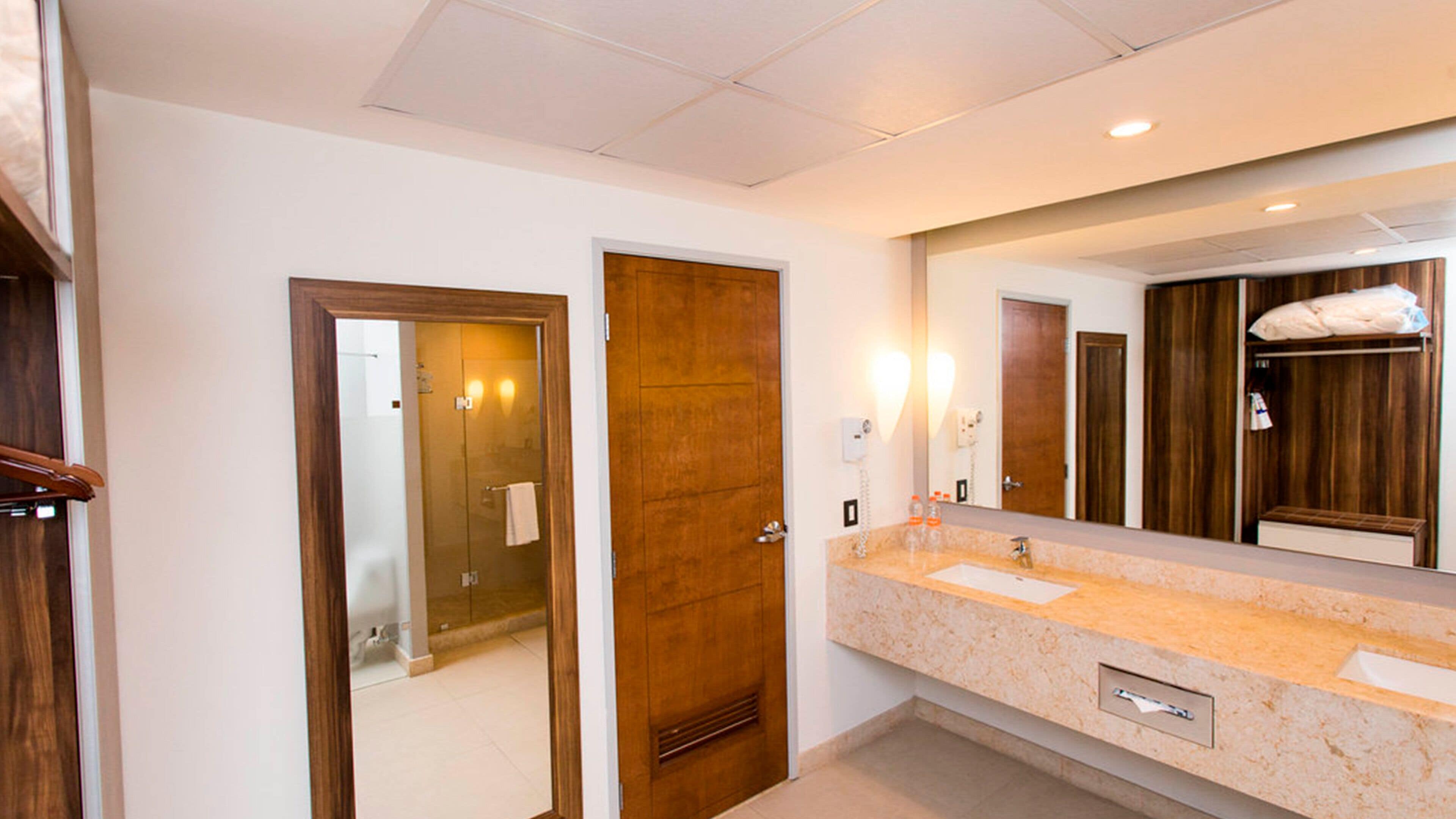 A hotel bathroom with a wooden door, a large mirror, a sink, and a towel rack.