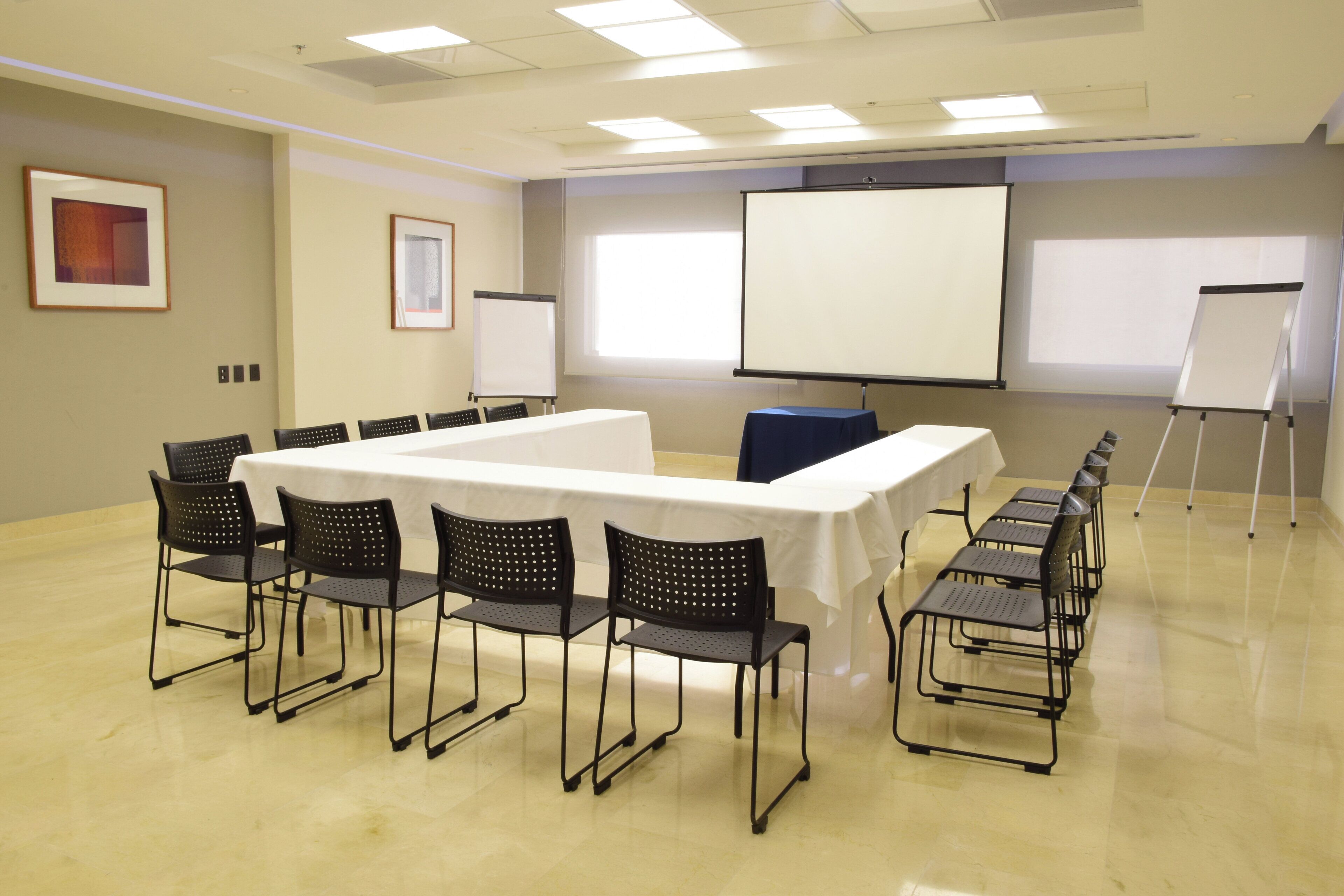 Un salón de conferencias con una mesa larga, sillas, una pantalla de proyector y una pizarra.