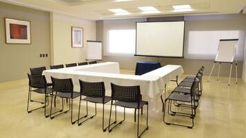 Un salón de conferencias con una mesa larga, sillas, una pantalla de proyector y una pizarra.