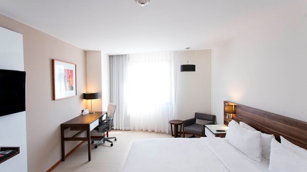 A hotel room with a large bed, a desk with a chair, a small table, and a TV mounted on the wall.
