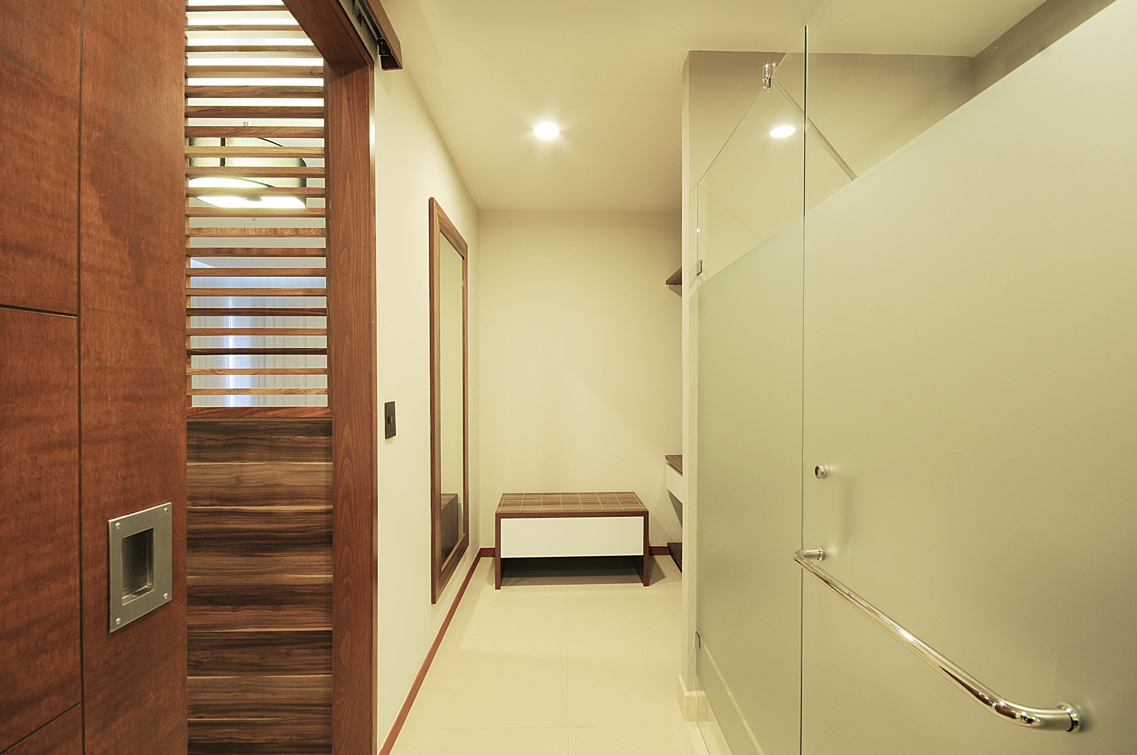 Une salle de bain moderne avec une douche à parois de verre, un banc en bois et une barre d’appui.