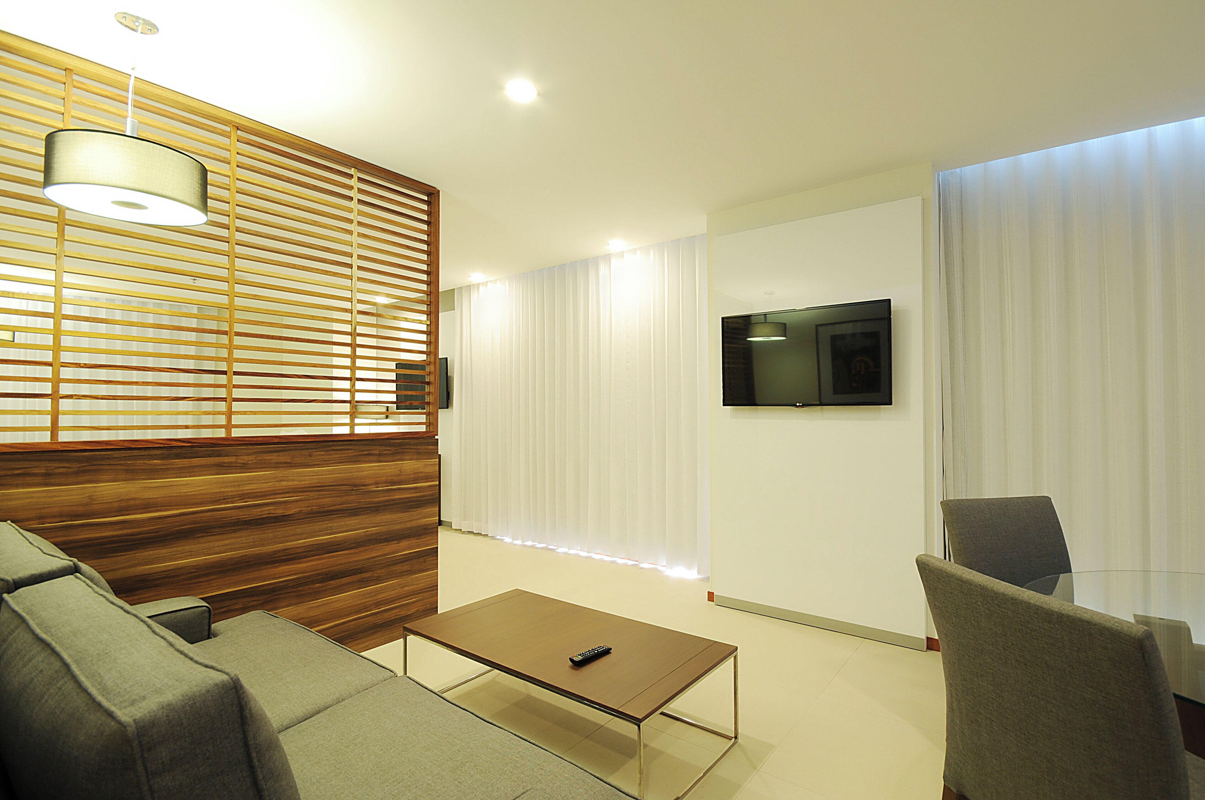 A modern living room with a sofa, a coffee table, a TV mounted on the wall, and a wooden slatted partition.