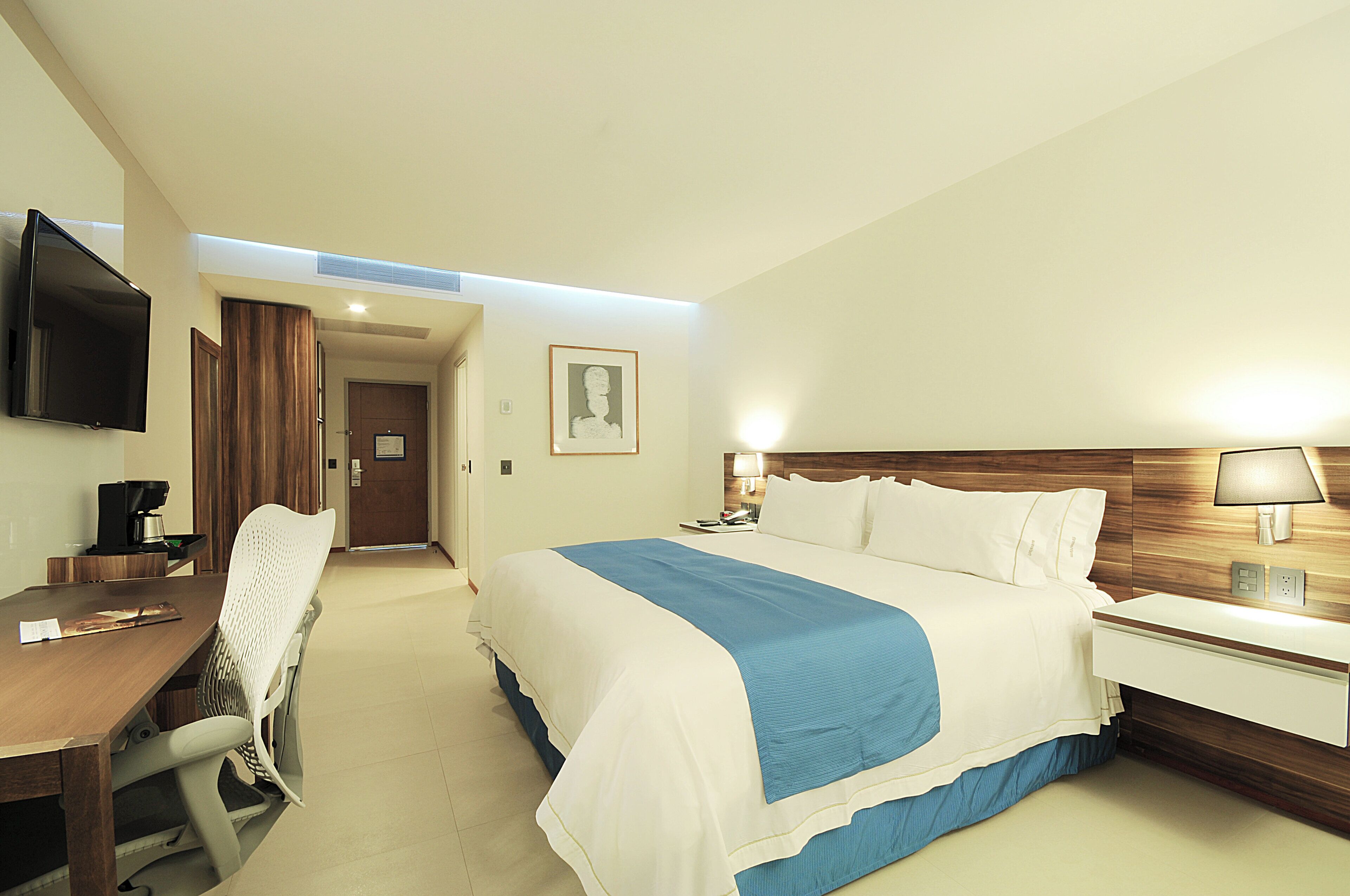 A hotel room with a bed, a desk, a chair, a television, and a door leading to another room.