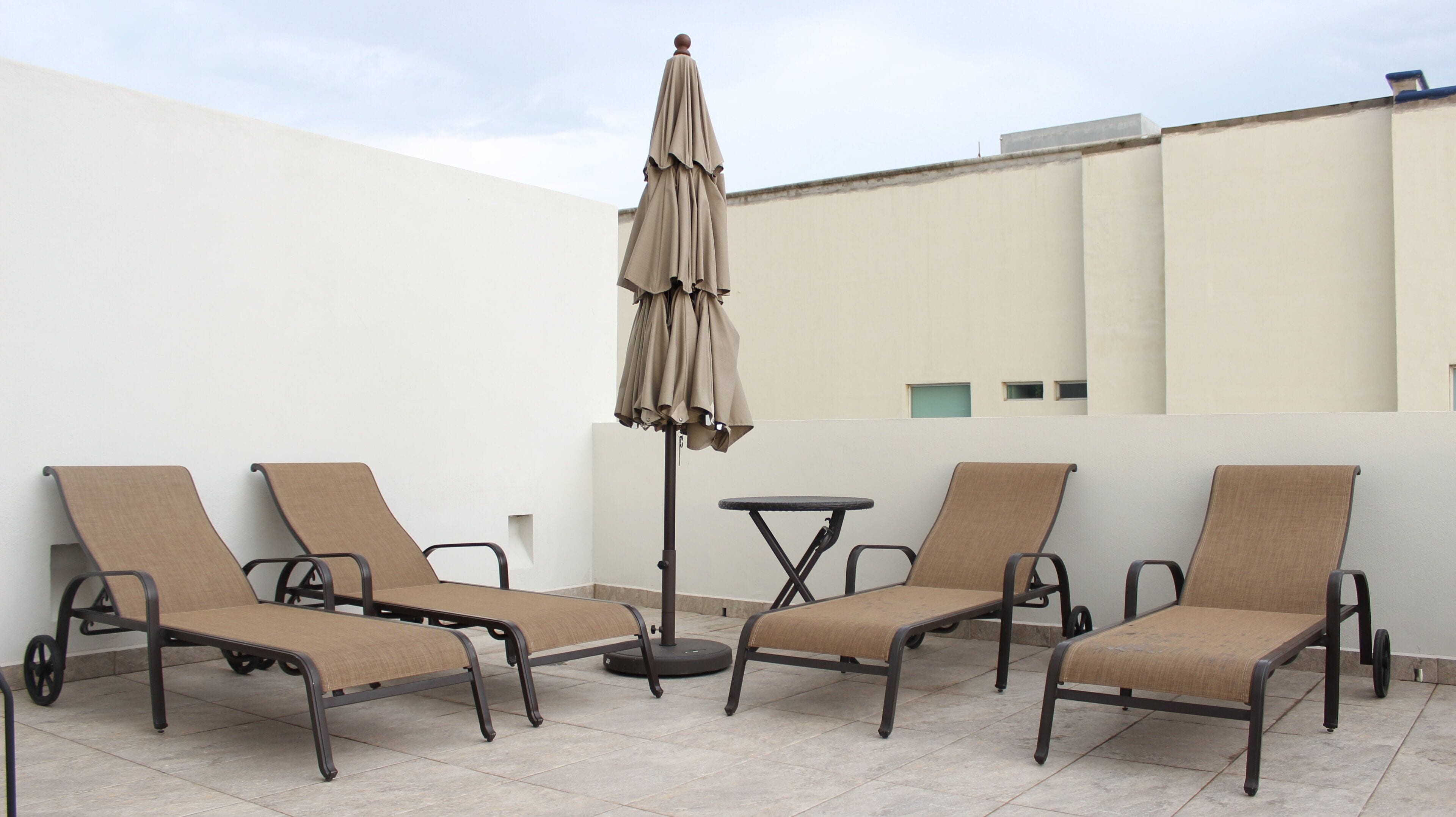 Une terrasse sur le toit, avec quatre chaises longues et une table, un parasol et une vue sur un immeuble.