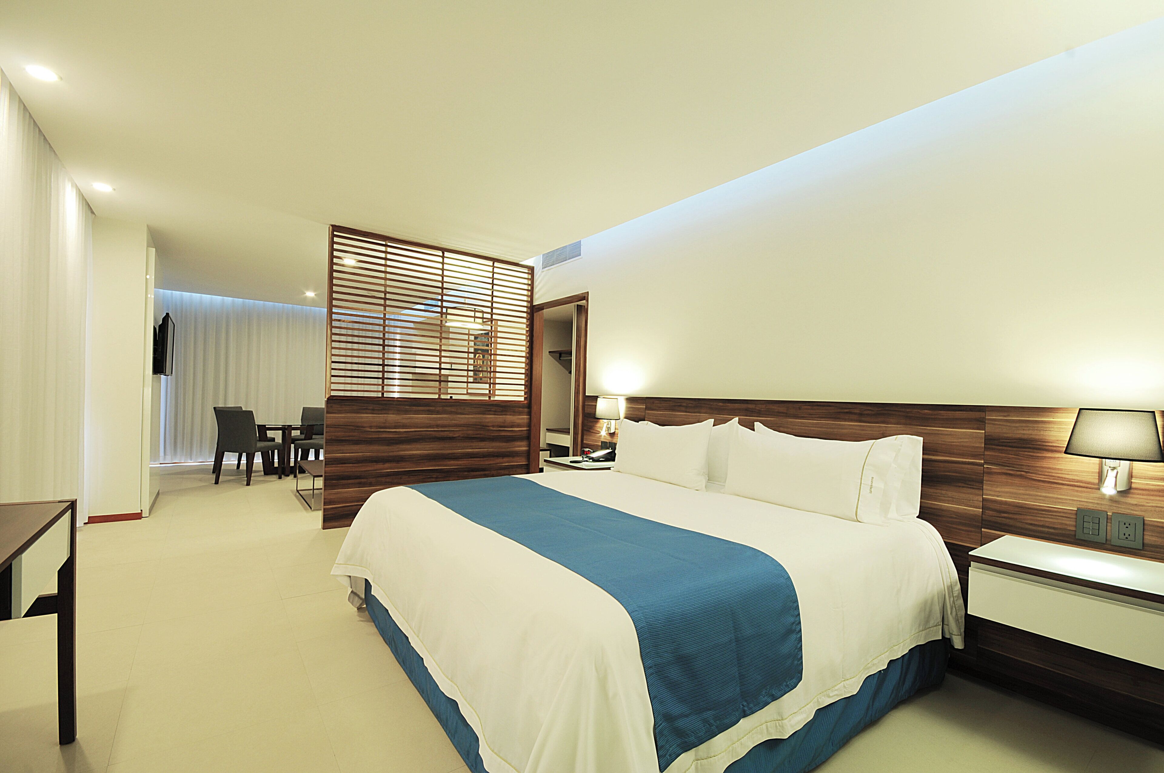 A hotel room with a large bed, bedside table, and a desk with a chair.