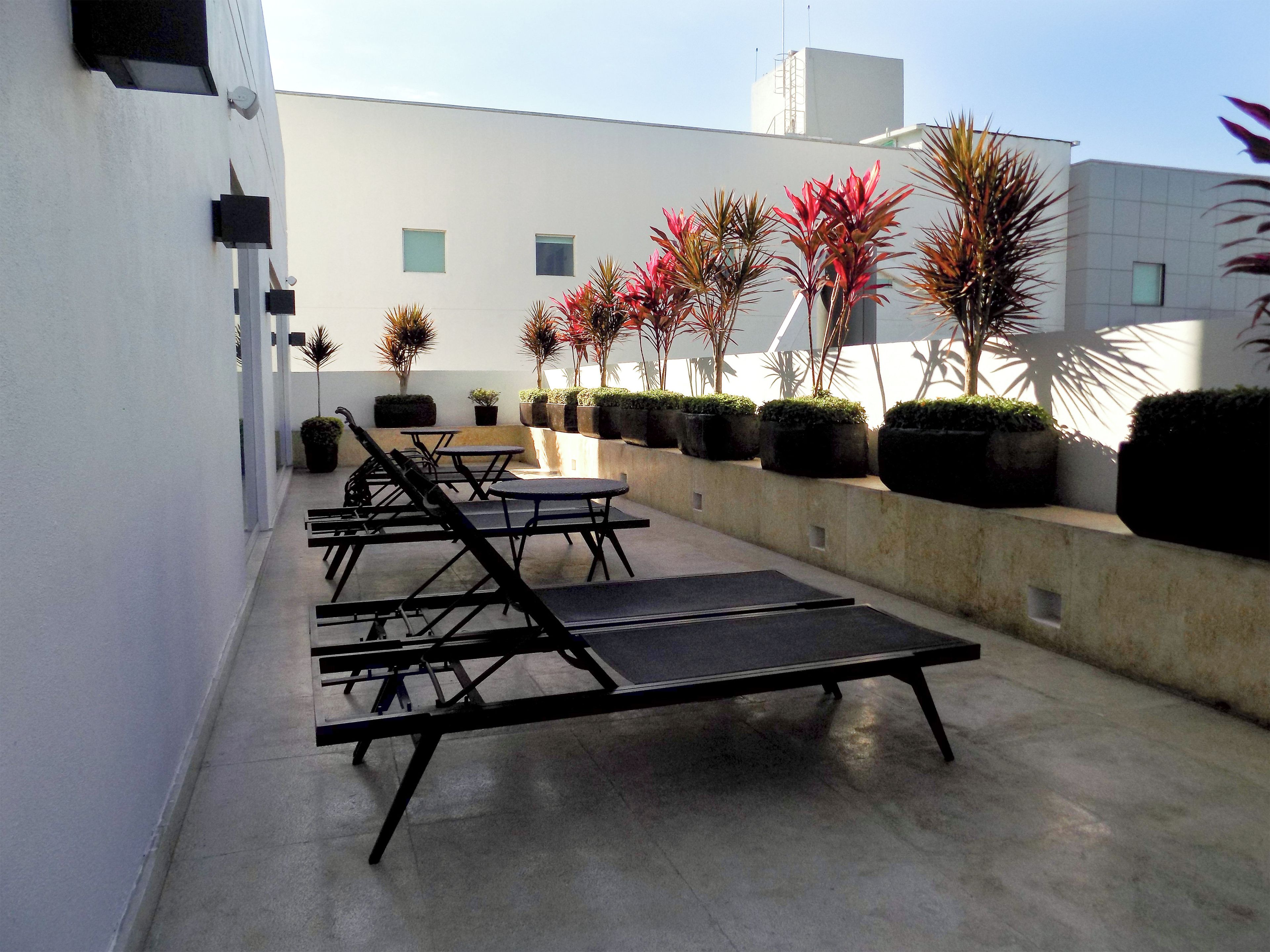 A rooftop terrace with lounge chairs, tables, and potted plants.