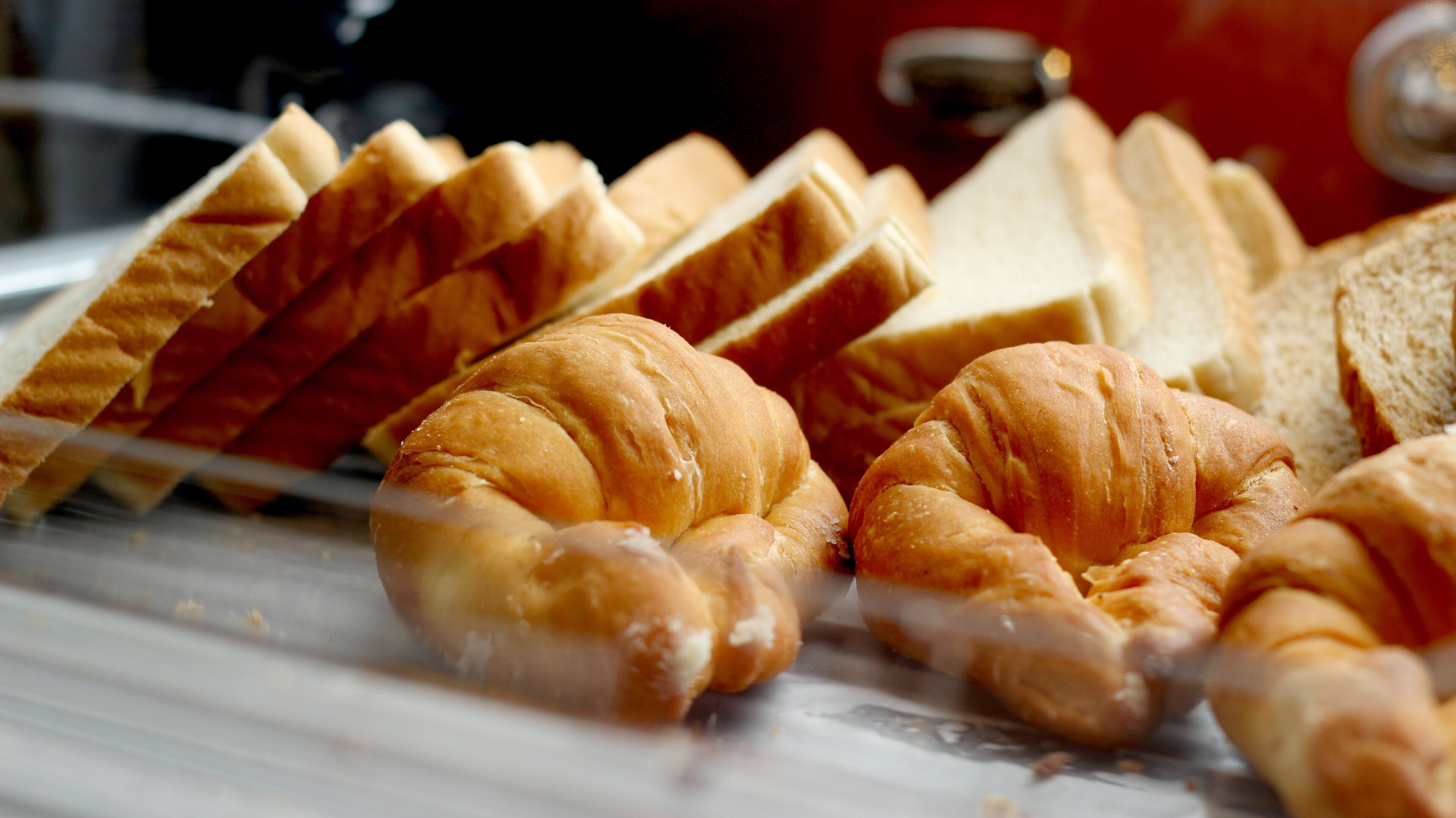 Diversos produtos de panificação, incluindo croissants e pão fatiado, expostos em uma padaria.