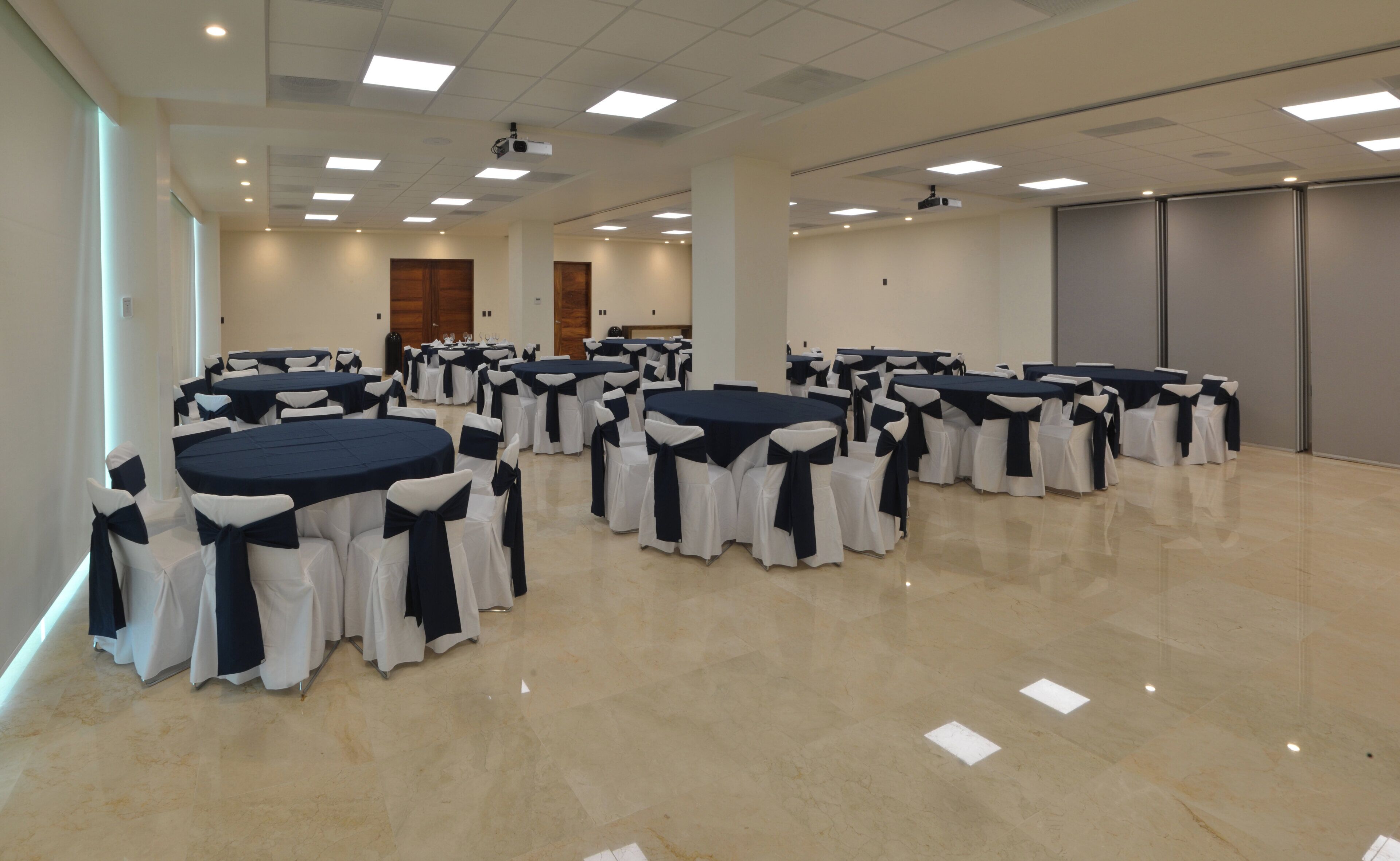Uma sala de conferências ampla, com várias mesas redondas, cada uma delas rodeada por cadeiras com fitas pretas, e um chão de mármore polido.
