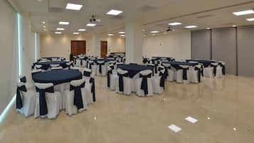 Uma sala de conferências ampla, com várias mesas redondas, cada uma delas rodeada por cadeiras com fitas pretas, e um chão de mármore polido.