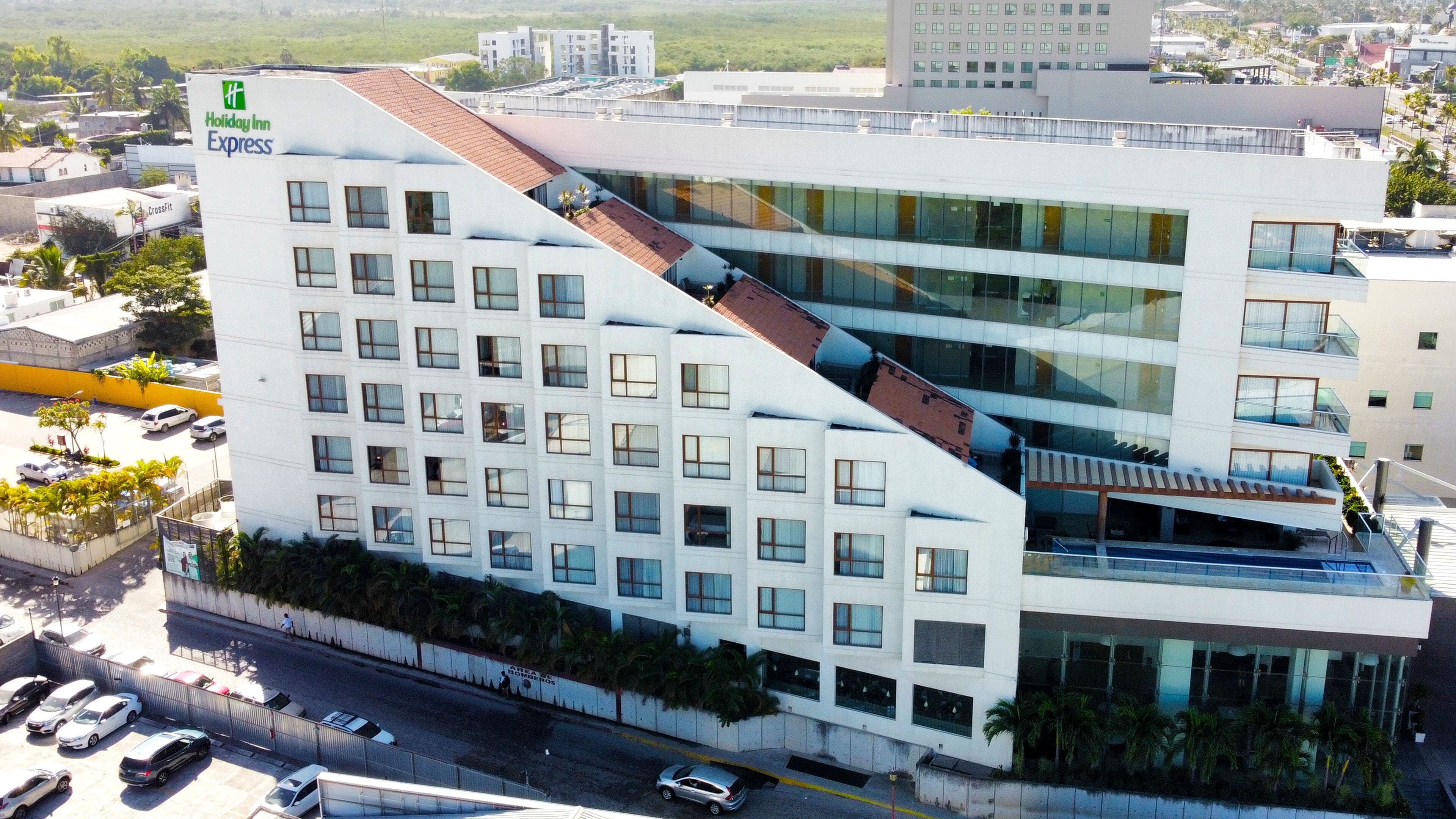 A modern Holiday Inn Express building with a unique sloped roof design, multiple floors, and a parking area visible below.