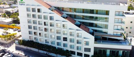 A modern Holiday Inn Express building with a unique sloped roof design, multiple floors, and a parking area visible below.