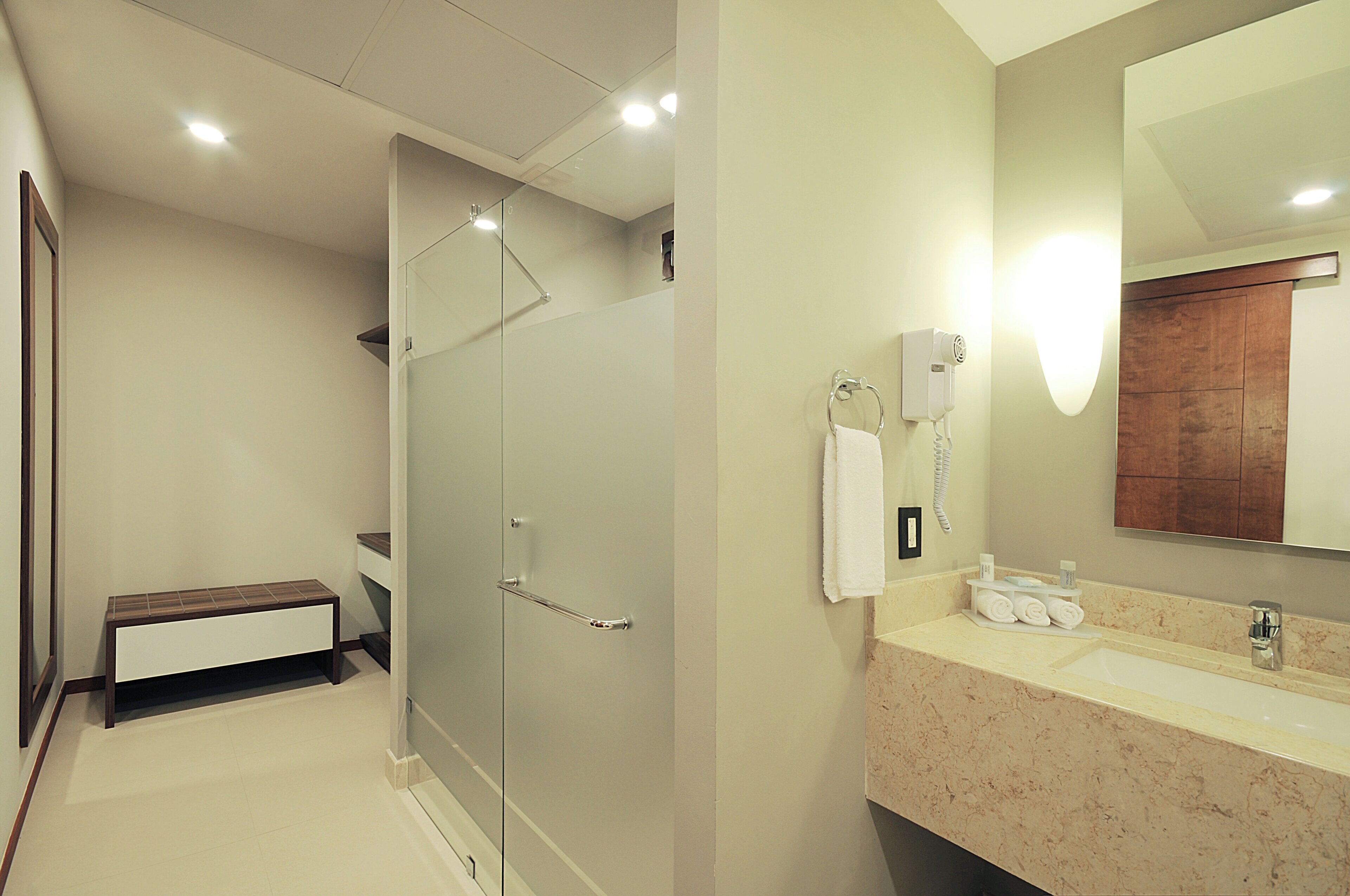 Une salle de bain moderne dotée d’une douche à parois de verre, d’un meuble-lavabo avec un plan de travail en marbre et d’un grand miroir.