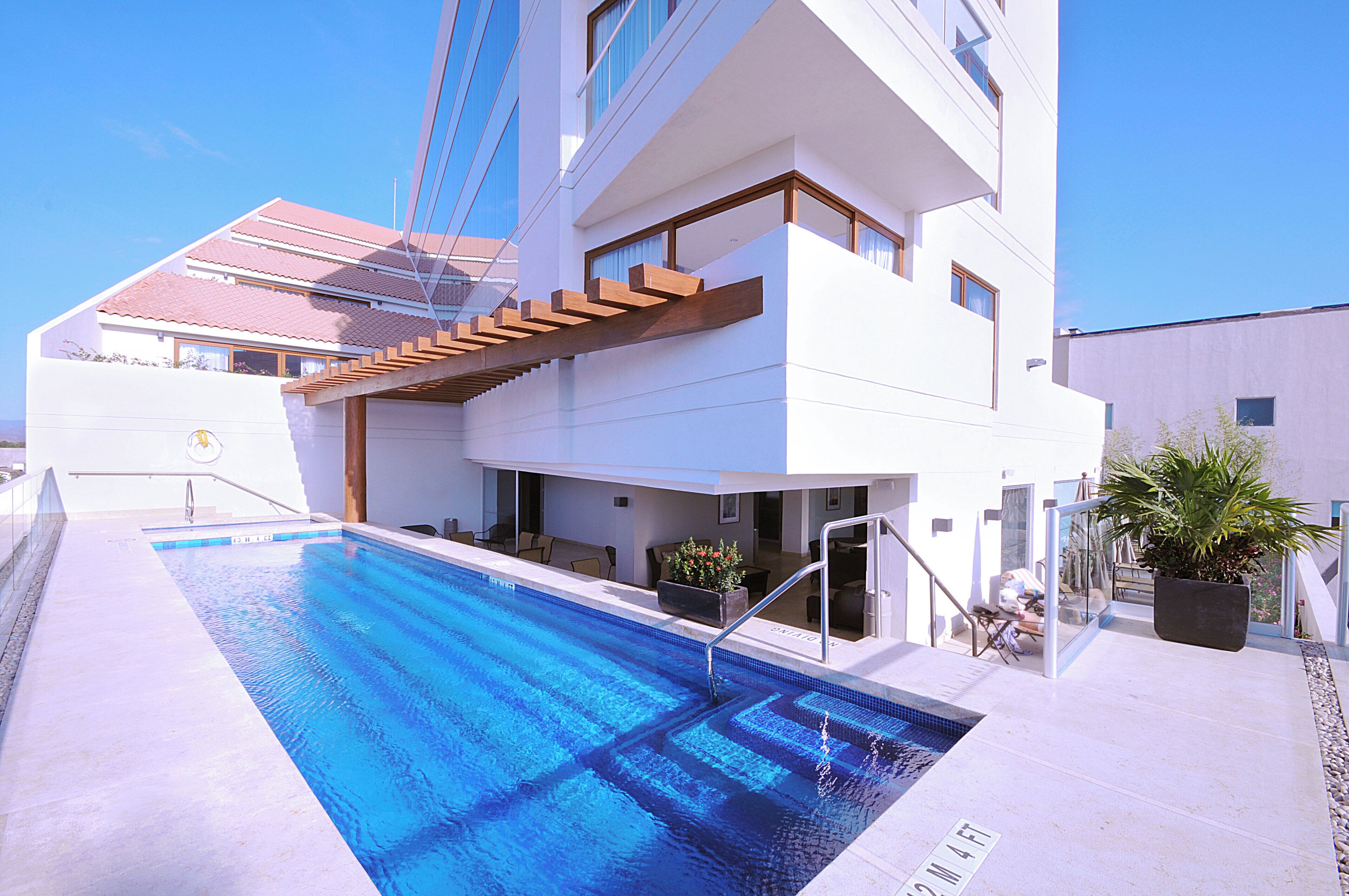 A modern hotel with a swimming pool, a covered outdoor seating area, and a view of the surrounding buildings.