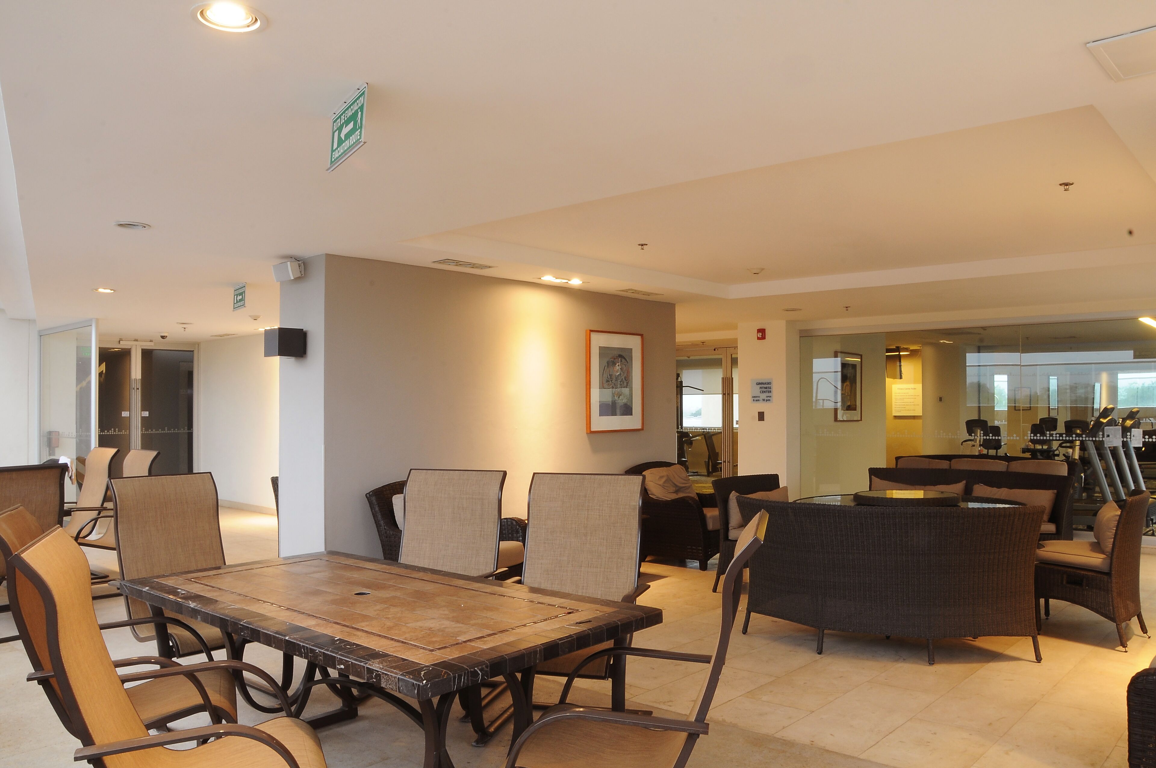 A spacious indoor area with a large wooden table surrounded by chairs, a round seating area, and a glass partition.