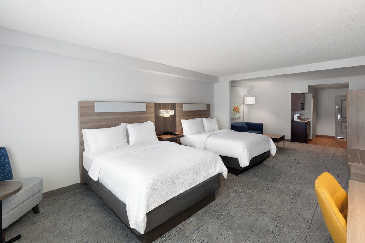 Une chambre d’hôtel avec deux lits, un bureau, une chaise et une petite kitchenette.