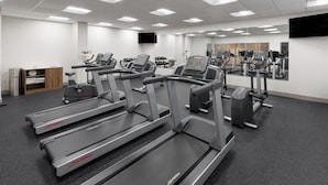 Une salle de sport équipée de tapis de course, d’haltères et d’un mur entièrement recouvert de miroirs.