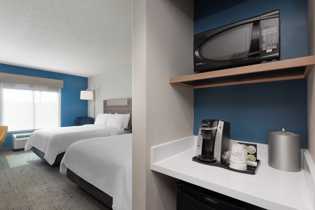 Une chambre d’hôtel avec deux lits, un four à micro-ondes, une machine à café et une poubelle.