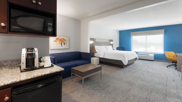 Une chambre d’hôtel avec une kitchenette, un lit, un canapé bleu, une machine à café et une grande fenêtre.