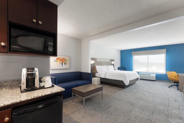 Une chambre d’hôtel avec une kitchenette, un lit, un canapé bleu, une machine à café et une grande fenêtre.
