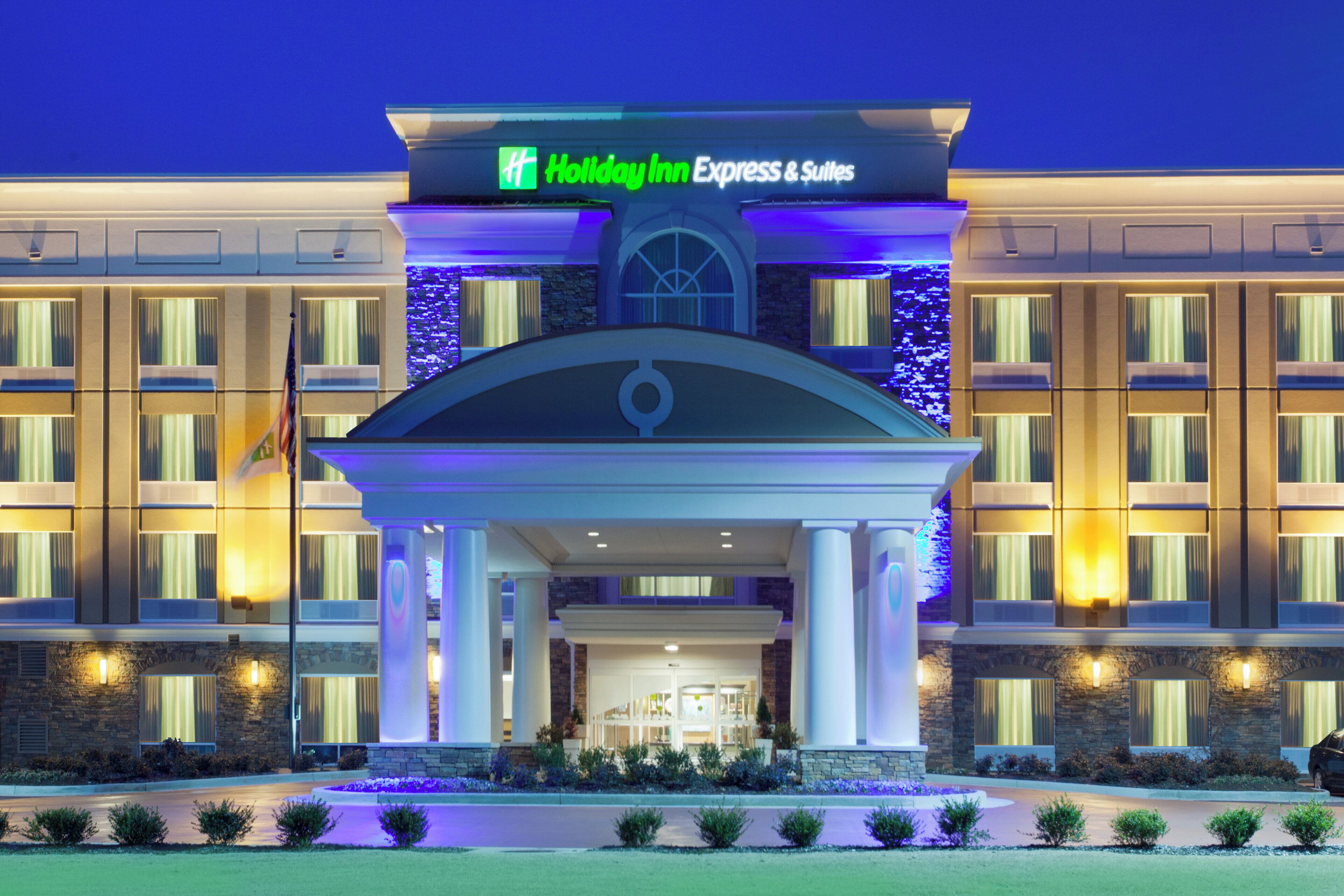 Un hotel Holiday Inn Express & Suites con fachada simétrica, amplias ventanas y una entrada central con arco decorativo.