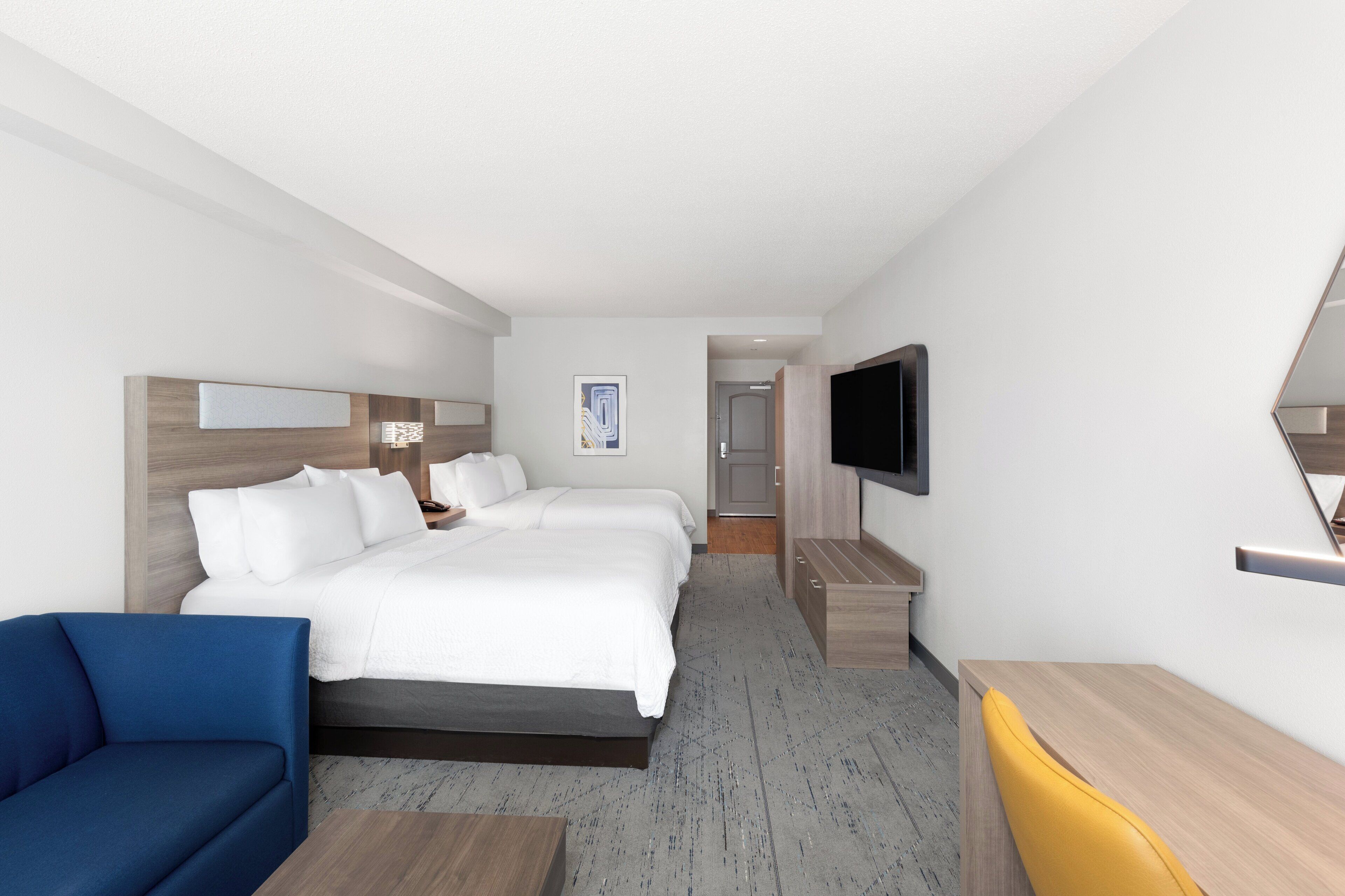 A hotel room with a large bed, a TV mounted on the wall, a desk, and a chair.