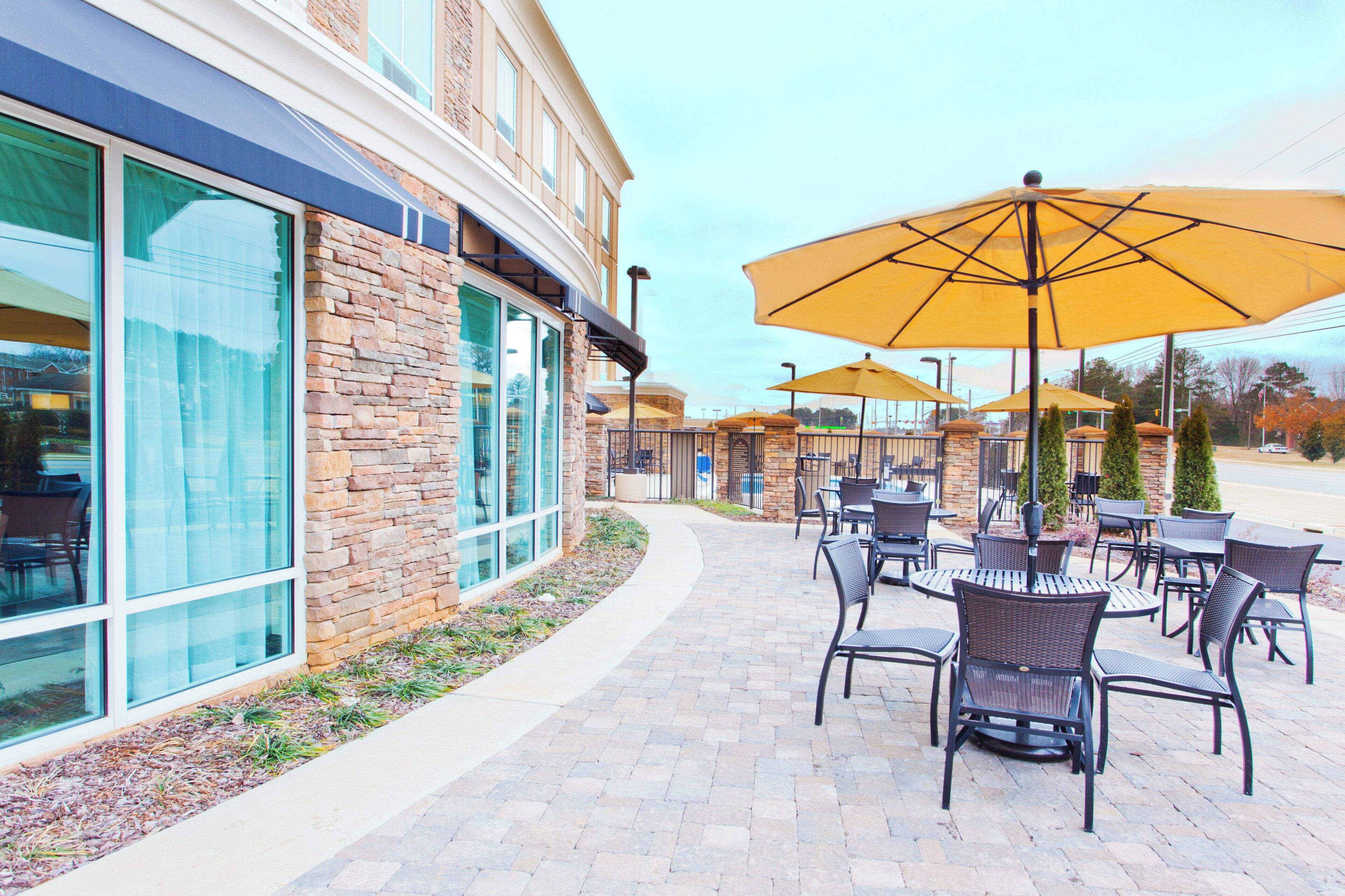 An outdoor patio area with brick flooring, outdoor seating with tables and chairs, and large umbrellas providing shade.
