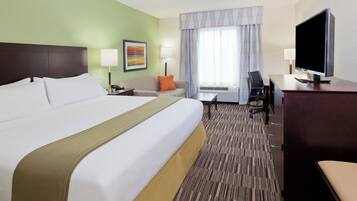 Une chambre d’hôtel avec un grand lit, un bureau, une chaise, une télévision et une fenêtre avec des rideaux.