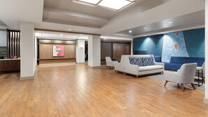 Eine geräumige Lobby mit Holzboden, einem Empfangstresen, einer blauen Wand mit einer Karte und einer Sitzecke mit einer Couch und Sesseln.