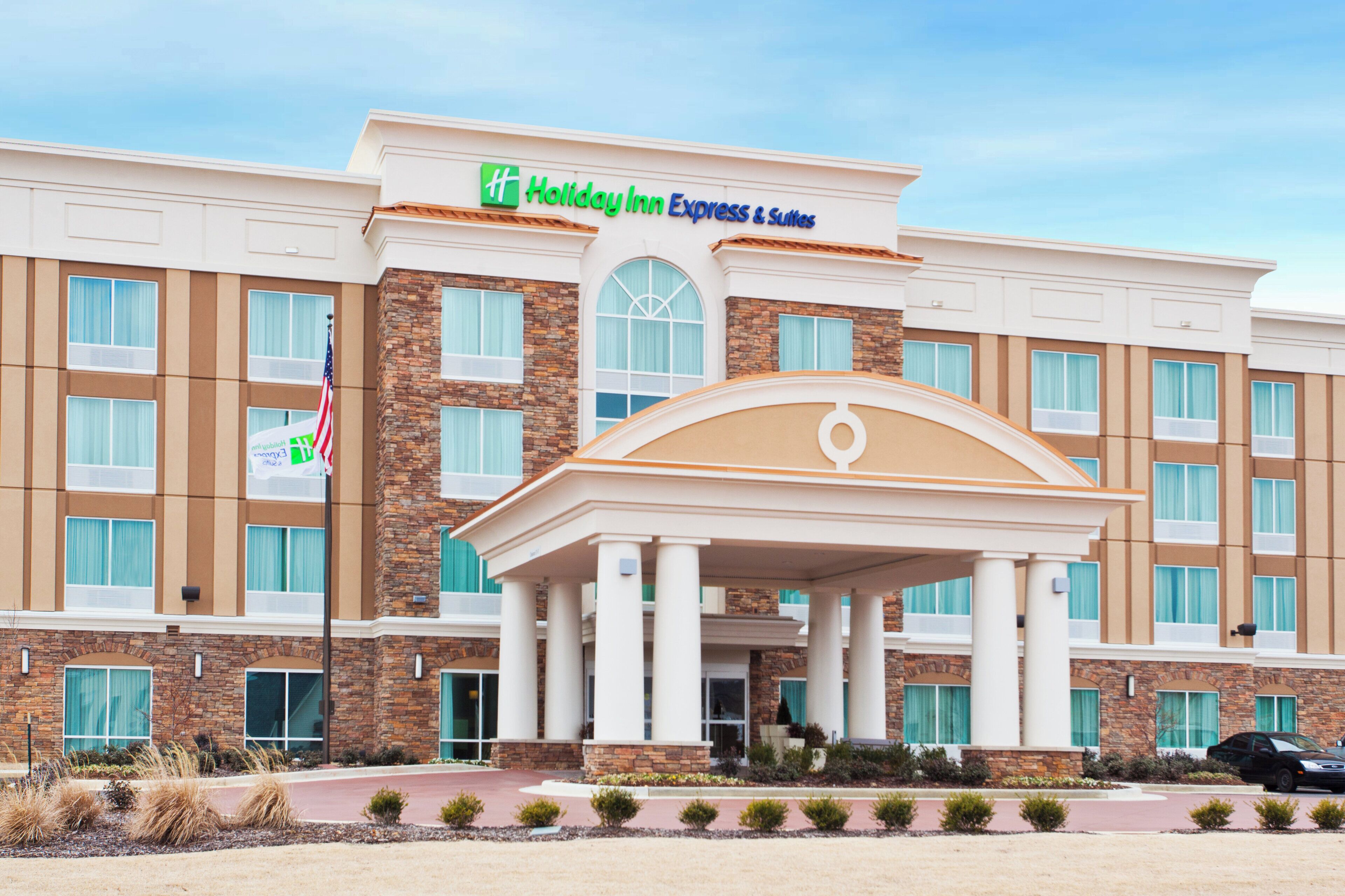 A Holiday Inn Express & Suites hotel with a central entrance, multiple windows, and a flag.
