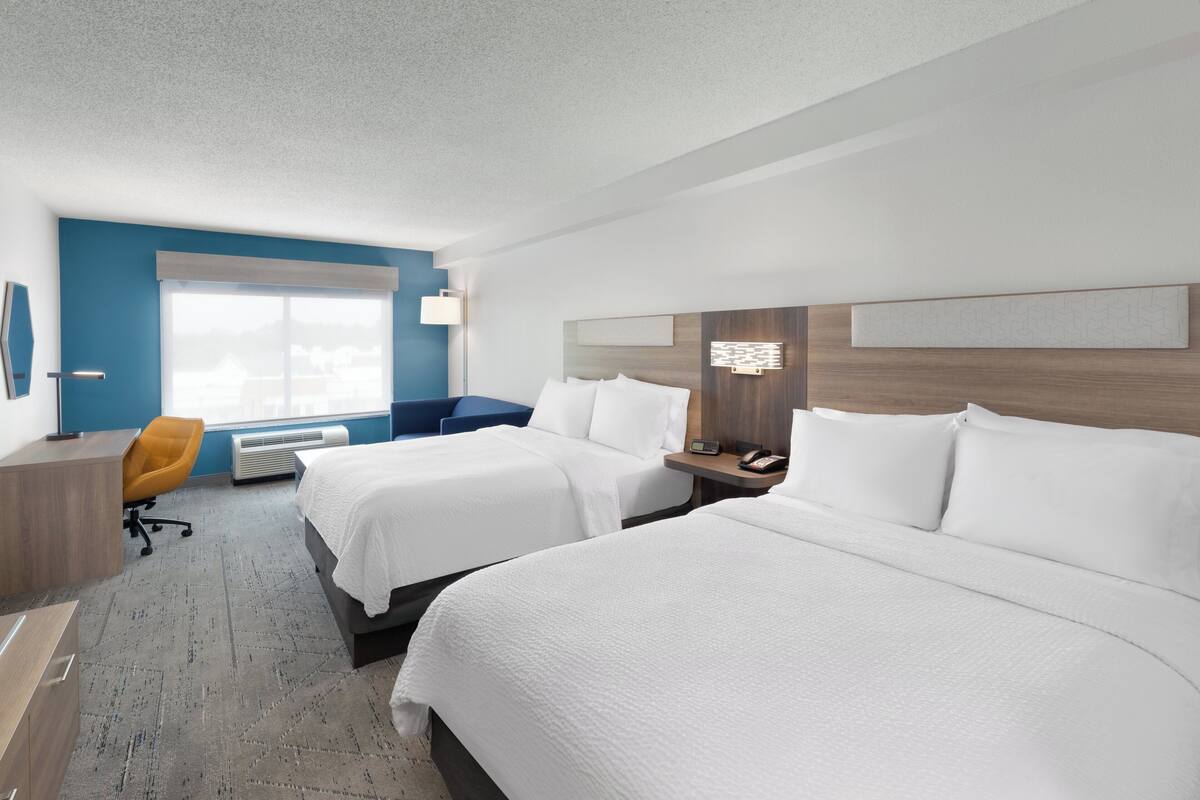 Ein Hotelzimmer mit zwei Betten, einem Schreibtisch, einem Stuhl und einem großen Fenster.