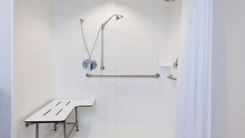Un espace douche moderne équipé d’une barre d’appui, d’un pommeau de douche à main et d’un drain au sol.