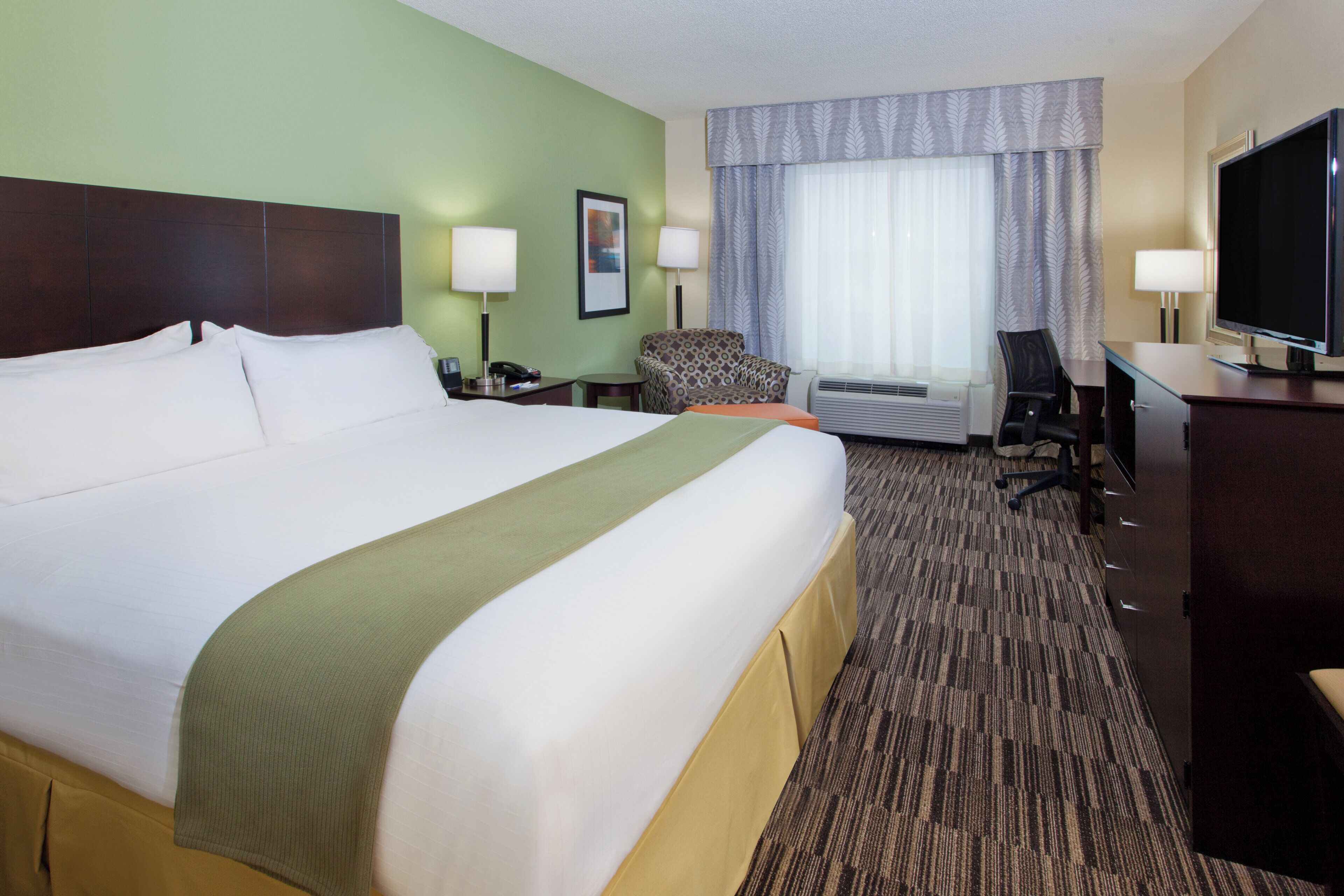 Een hotelkamer met een groot bed, een bureau, een stoel, een televisie en een raam met gordijnen.