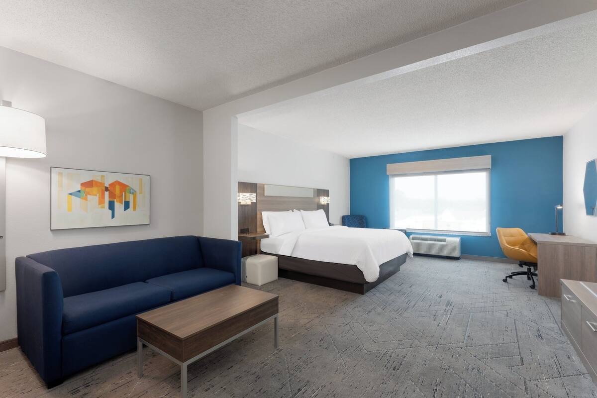 Ein Hotelzimmer mit einem Bett, einem blauen Sofa, einem Holztisch, einem Schreibtisch und einem Stuhl.