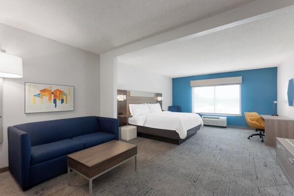 A hotel room with a bed, a blue sofa, a wooden coffee table, a desk, and a chair.
