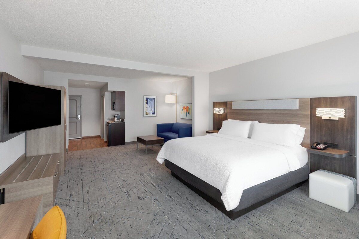 Une chambre d’hôtel moderne dotée d’un grand lit, d’un téléviseur à écran plat, d’un bureau et d’un coin salon avec un fauteuil bleu.