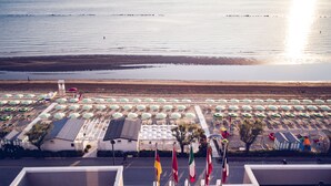 A beachside hotel with rows of umbrellas and beach chairs, a lifeguard tower, and flags. - UNAWAY Imperial Beach Fano (Fano)