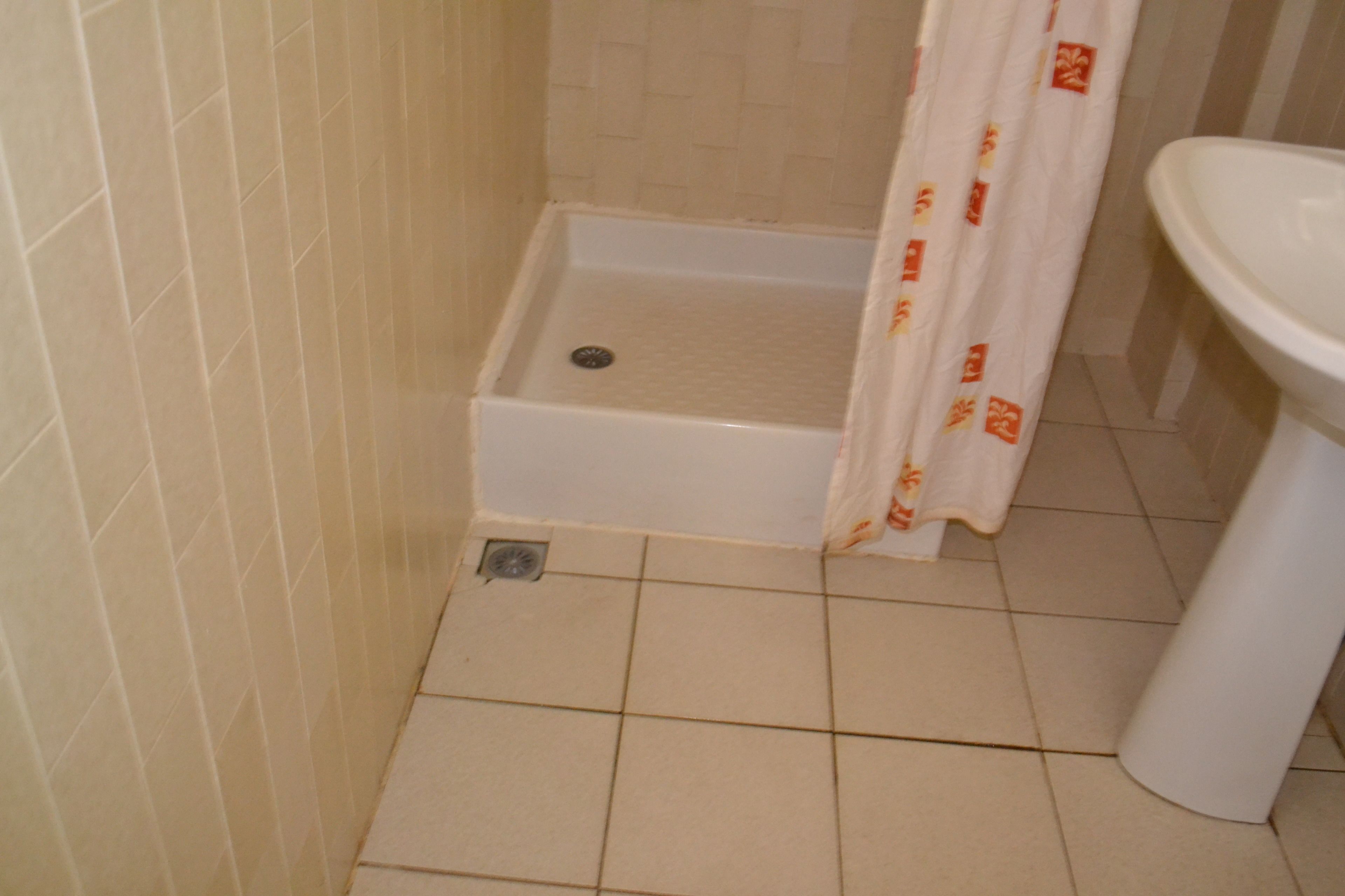 Un baño con ducha, lavamanos y suelo de baldosas.