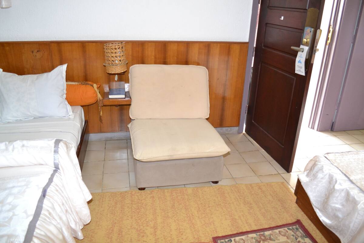 A hotel room with a bed, a small sofa, a nightstand, and a door.