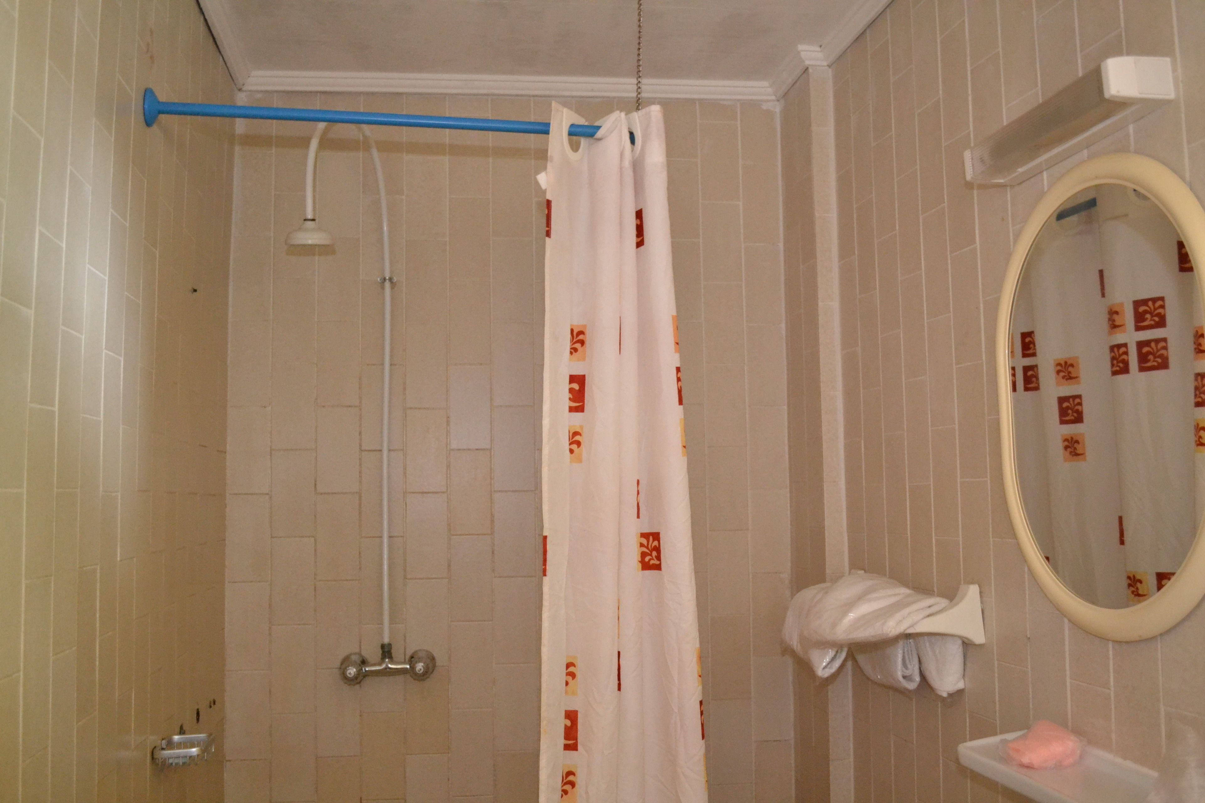 A bathroom with a shower, a towel rack, a mirror, and a shelf with a soap dispenser.