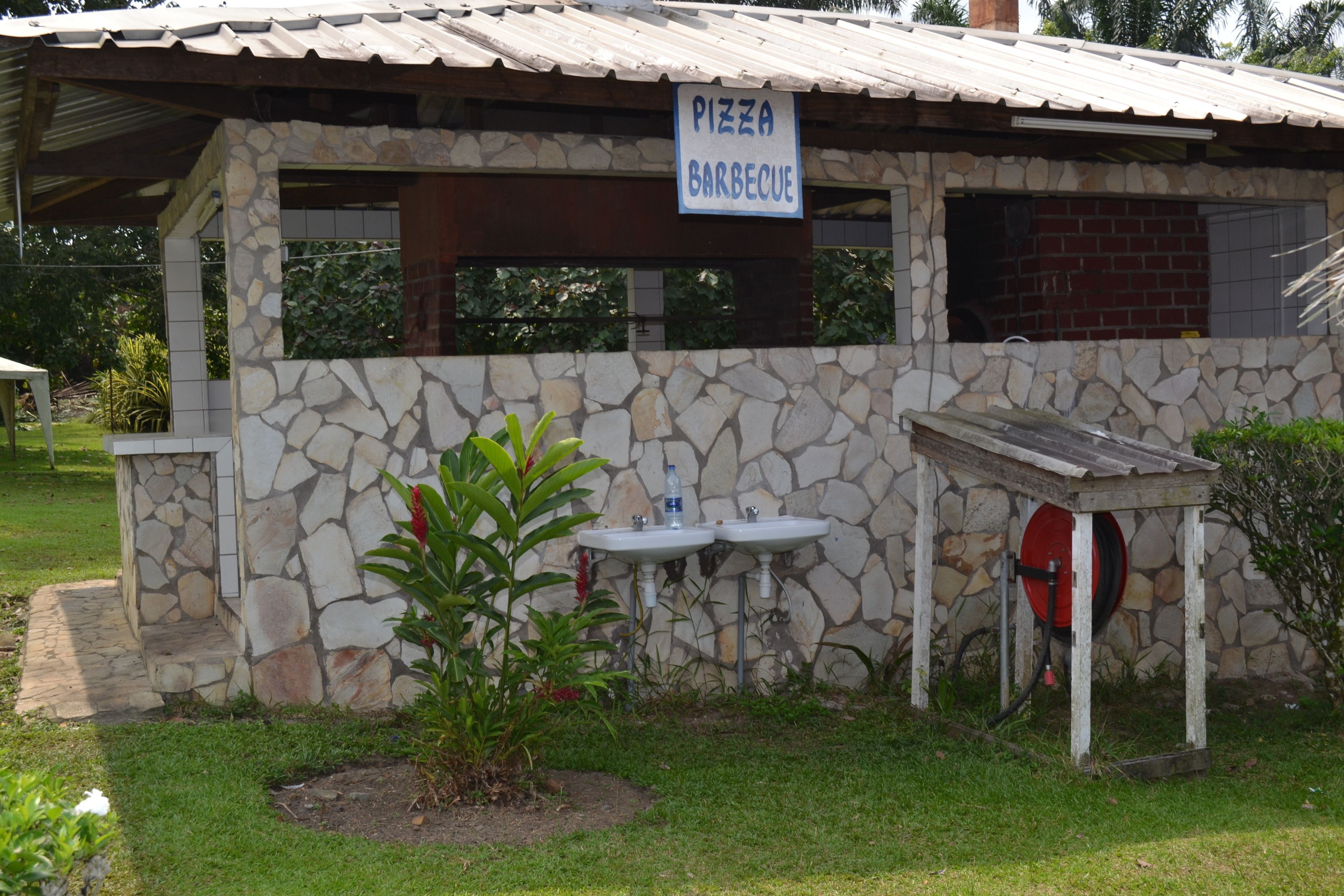 A stone building with a sign reading "Pizza Barbecue," two outdoor sinks, and a hose.