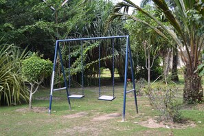 Eine Schaukel im Garten mit dichtem Grün und Bäumen im Hintergrund.