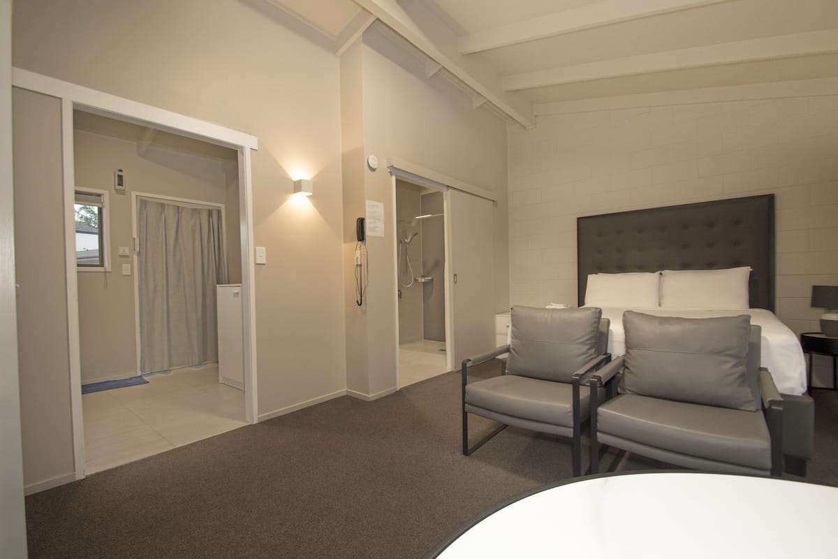 A hotel room with a bed, a chair, a desk, and a shower area.